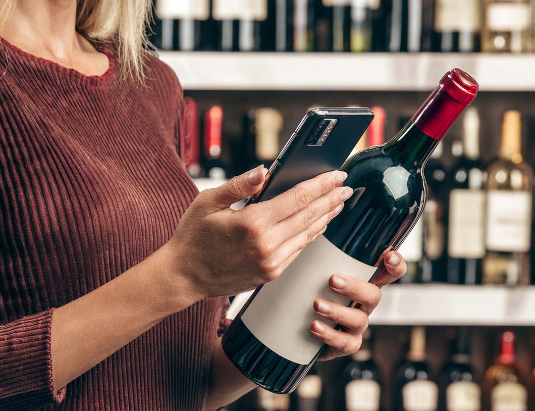 Una donna che legge l’etichetta della bottiglia di vino attraverso l’uso della tecnologia NFC.
